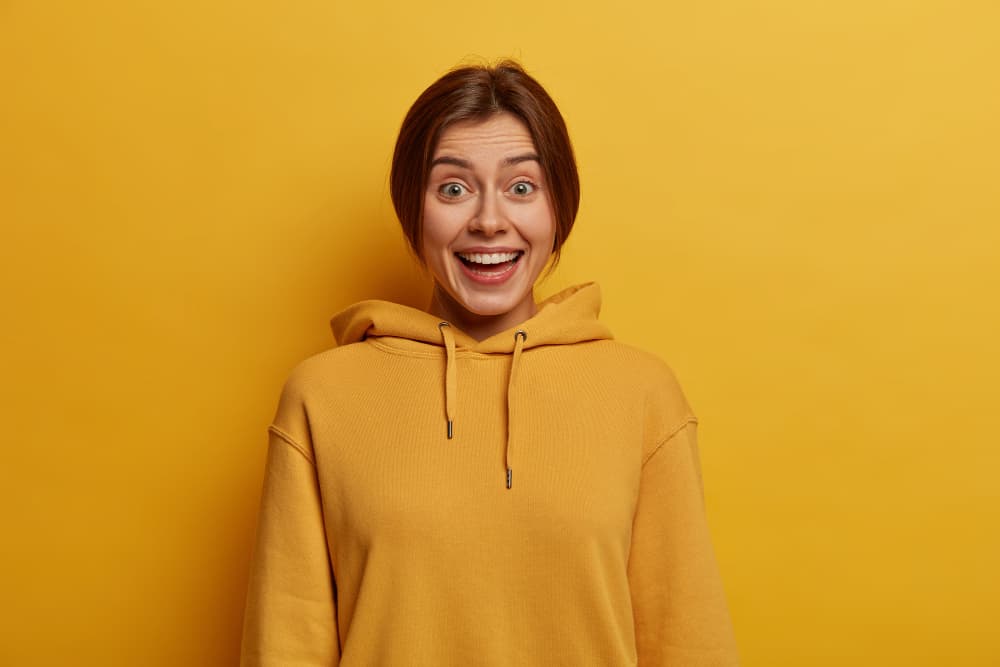 Brown haired girl wearing yellow blank hoodie laughing happily